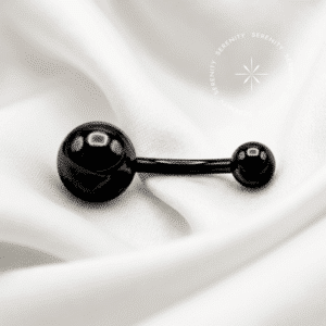 Piercing Umbigo Titânio Black repousando suavemente sobre um tecido de cetim preto de alta opulência, evidenciando o contraste entre a haste escura e o brilho intenso da zircônia central.