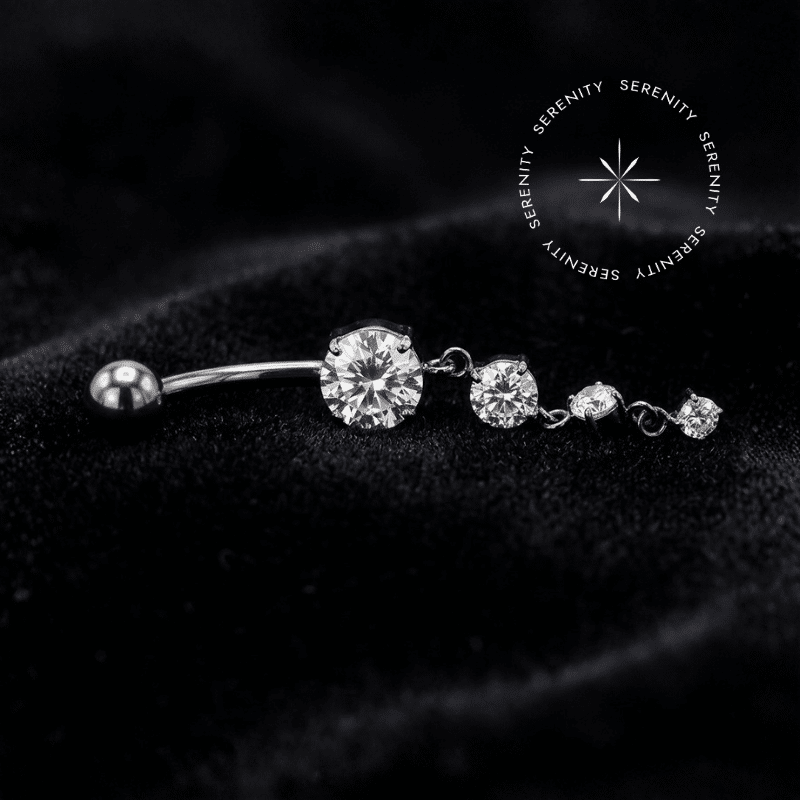 Piercing Umbigo Titânio Cascata Cravejado contendo três Zircônias Translúcidas de Lapidação Premium com haste curva em Titânio Grau Implante, repousando suavemente sobre um tecido de cetim branco de alta opulência.
