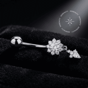 Piercing umbigo titânio em formato de flor com pendente inferior, inteiramente cravejado com zircônias translúcidas, haste curva e rosca interna, repousando suavemente sobre um tecido de cetim branco de alta opulência.
