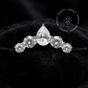 piercing titânio grau implante modelo cluster com gota central cravejada repousando suavemente sobre um tecido de cetim branco de alta opulência.
