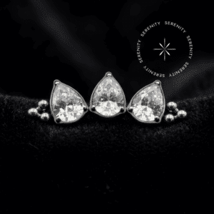 piercing titânio grau implante modelo cluster com 3 gotas e esferas cravejado de zircônias translúcidas repousando suavemente sobre um tecido de cetim branco de alta opulência.