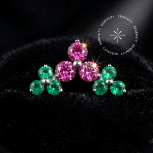 piercing titânio grau implante modelo cluster trinity cravejado com zircônias rosa e verde, repousando suavemente sobre um tecido de cetim branco de alta opulência.