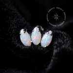 piercing titânio grau implante modelo topo mini cluster opala cravejado com gemas brancas, repousando suavemente sobre um tecido de cetim branco de alta opulência.