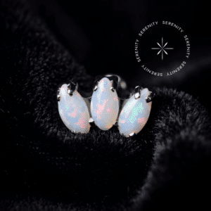 piercing titânio grau implante modelo topo mini cluster opala cravejado com gemas brancas, repousando suavemente sobre um tecido de cetim branco de alta opulência.