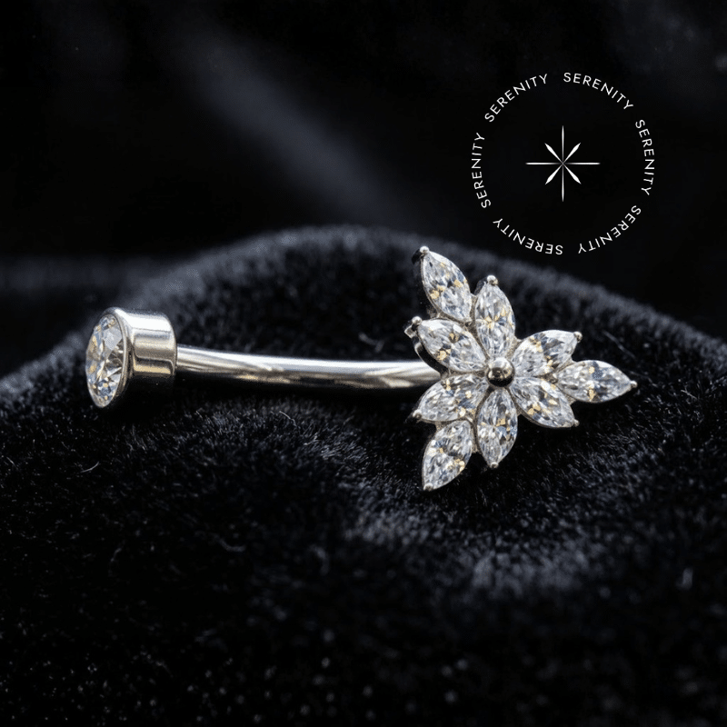 piercing umbigo titânio com arranjo triangular em zircônias translúcidas formato navete de lapidação premium, repousando suavemente sobre um tecido de cetim branco de alta opulência evidenciando o polimento espelhado impecável do metal grau implante.