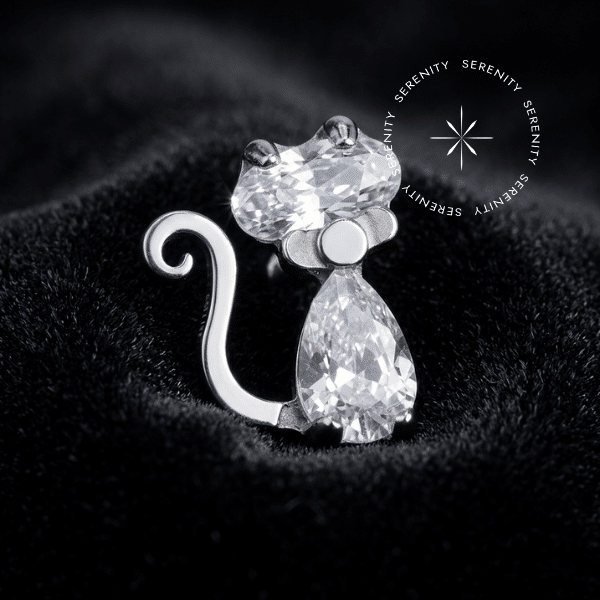 Piercing Titânio Grau Implante com topo figurativo em formato de gato de 5.5mm x 4.2mm e Zircônias Premium em lapidação coração e gota na cor Translúcido Majestic. Apresenta pino inferior compatível com rosca interna atraumática de 0.9mm. Uma peça de alta joalheria corporal projetada para cartilagens e lóbulo, oferecendo estética de luxo afetuosa e cicatrização segura.