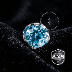 Piercing Ponto de Luz Titânio TT18 com sistema push pin e Zircônia Premium azul aqua, exibindo o selo de verificação técnica da Titânio Mill APP Phase 1.