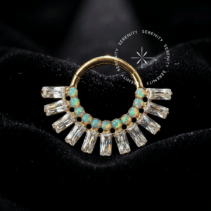 Argola Frontal Baguetes Opala utilizada como piercing, forjada em Titânio Revestido de Ouro 18k com coroa geométrica de zircônias transparentes e opalas sintéticas, fotografada em fundo claro.