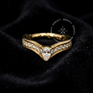 Argola Lateral Gota Central utilizada como piercing, forjada em Titânio Revestido de Ouro 18k com coroa cravejada no aro externo em formato de V e zircônia em formato de gota, fotografada em fundo claro.
