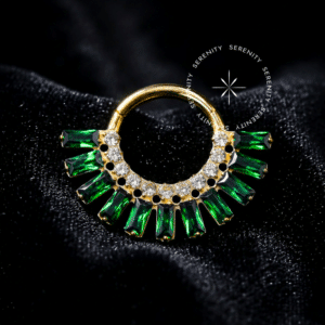 Piercing tipo Argola Frontal Luxo Baguetes Cores Frontal em Titânio Revestido de Ouro 18k com coroa de zircônias baguetes intercaladas em verde esmeralda e cristal, em fundo claro.