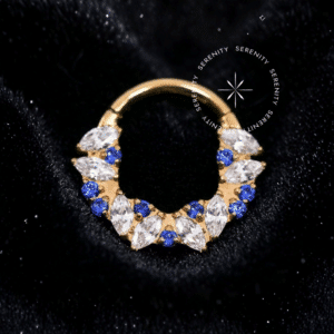 Piercing tipo Argola Frontal Coroa Safira em Titânio Revestido de Ouro 18k com design de coroa em zircônias premium azul safira e cristais transparentes, em fundo claro.