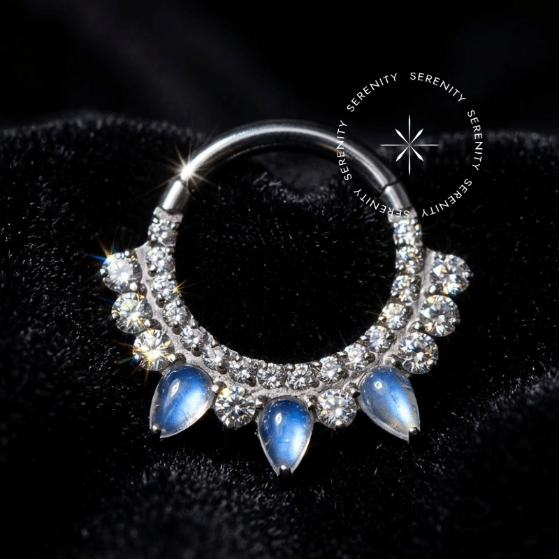 piercing septo titânio em formato de argola clicker prateada com cravação frontal. Possui três pedras navetes sintéticas moonstone centrais ladeadas por pequenas zircônias cristal, formando um design de coroa, ideal para daith e septo.
