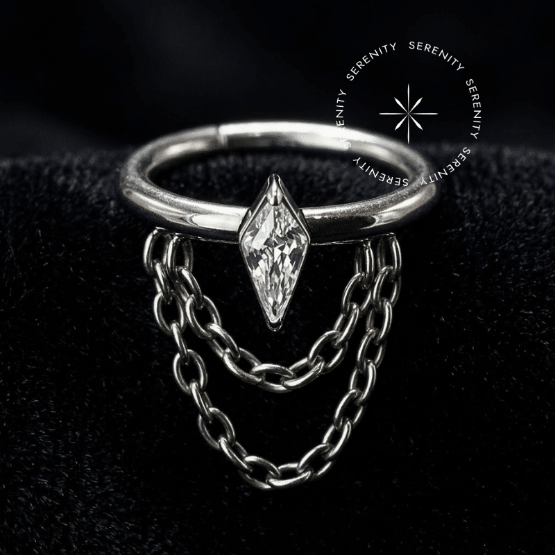 argola click titânio com design lateral apresentando uma Zircônia Premium Navete central e três delicadas correntes fluidas em cascata, textura majestosa projetada em alto contraste sobre cetim, equipada com mecanismo articulado clicker, perfeitamente ideal para anatomia de hélix e conch.