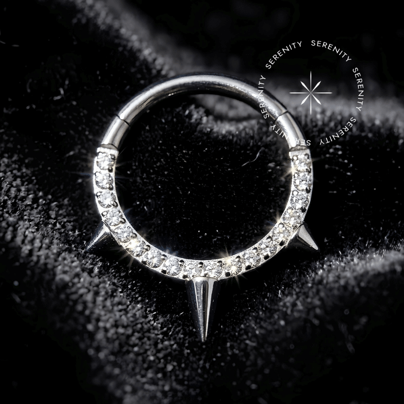 argola septo titânio com design de borda frontal cravejada por zircônias brilhantes e um espinho central spike liso, sistema de fecho clicker articulado em metal de grau médico hipoalergênico.