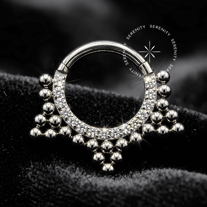 Argola Septo Titânio esculpida com coroa de esferas sólidas texturizadas e cravação estritamente frontal de Zircônia Premium Radiante. Equipada com pino articulado tipo clicker, refletindo alto luxo, ideal para harmonização anatômica em perfurações de septo e daith.