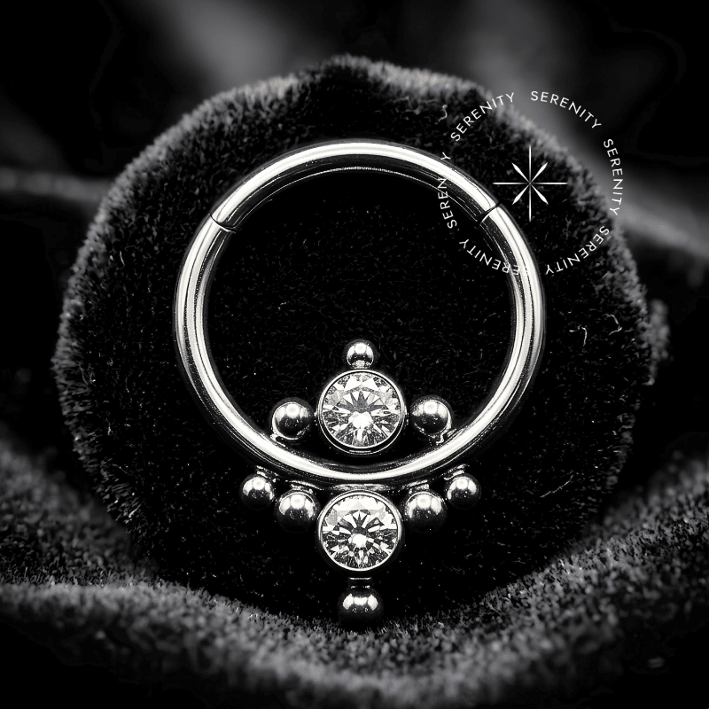Argola Septo Titânio com design frontal adornado com Zircônias Premium ladeadas por esferas texturizadas, fecho clicker de alta precisão anatômica, ideal para perfurações de septo e daith.