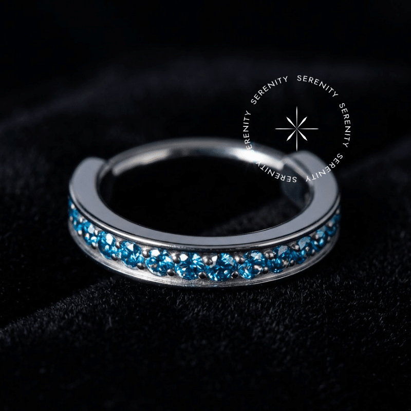 Argola Septo Titânio prateada de alto luxo, exibindo cravação frontal de zircônias premium na cor azul aqua vibrante, equipada com fecho clicker de dobradiça invisível, projetada estritamente para perfurações de septo e daith.