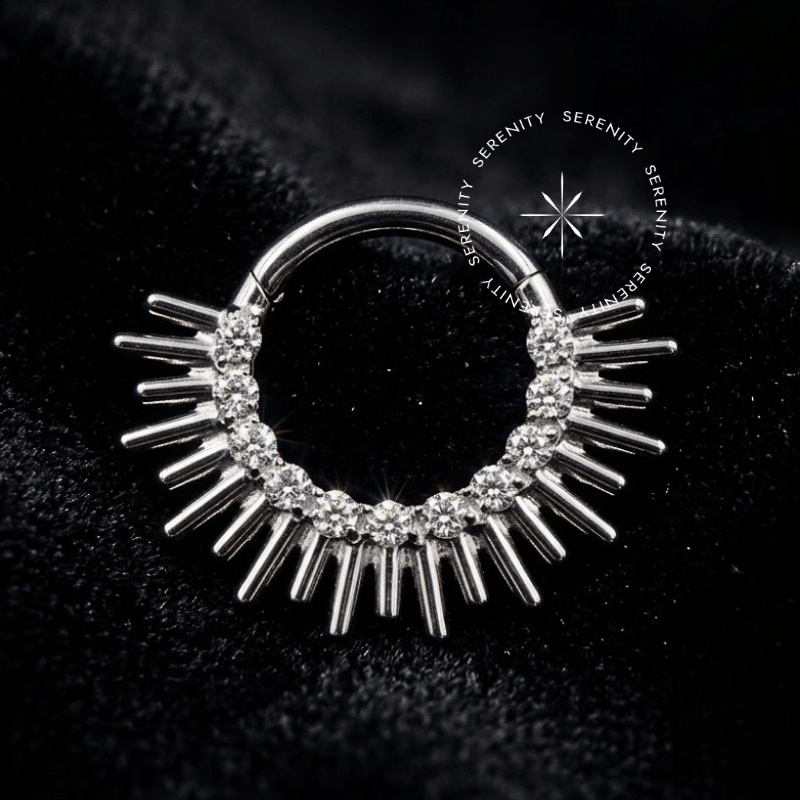 Argola Click Titânio cravejada frontalmente com zircônias premium em corte baguete formando raios em titânio natural prateado com pino clicker articulado, ideal para perfurações de septo e daith.