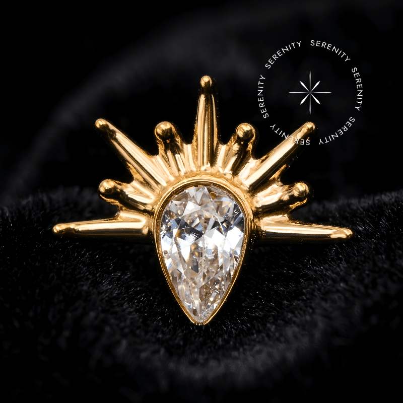 Piercing titânio dourado com design de gota irradiante e raios esculturais, fecho em rosca interna compatível com labret, ideal para curadoria luxuosa em cartilagens como helix e flat.
