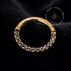 Argola clicker ouro 18k com cravação frontal de Zircônias Premium Ônix dispostas em pavé no metal de titânio dourado, mecanismo articulado, repousando de forma imponente, da exclusiva marca Serenity.