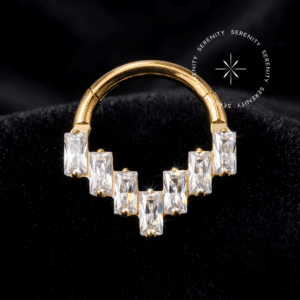 argola septo titânio dourado com design geométrico frontal triangular cravejado de pedras zircônia baguete translúcidas altamente reflexivas, haste com sistema de encaixe articulado clicker, repousando sobre um luxuoso fundo de tecido cetim branco puro, ideal para perfurações frontais de destaque como septo e daith.