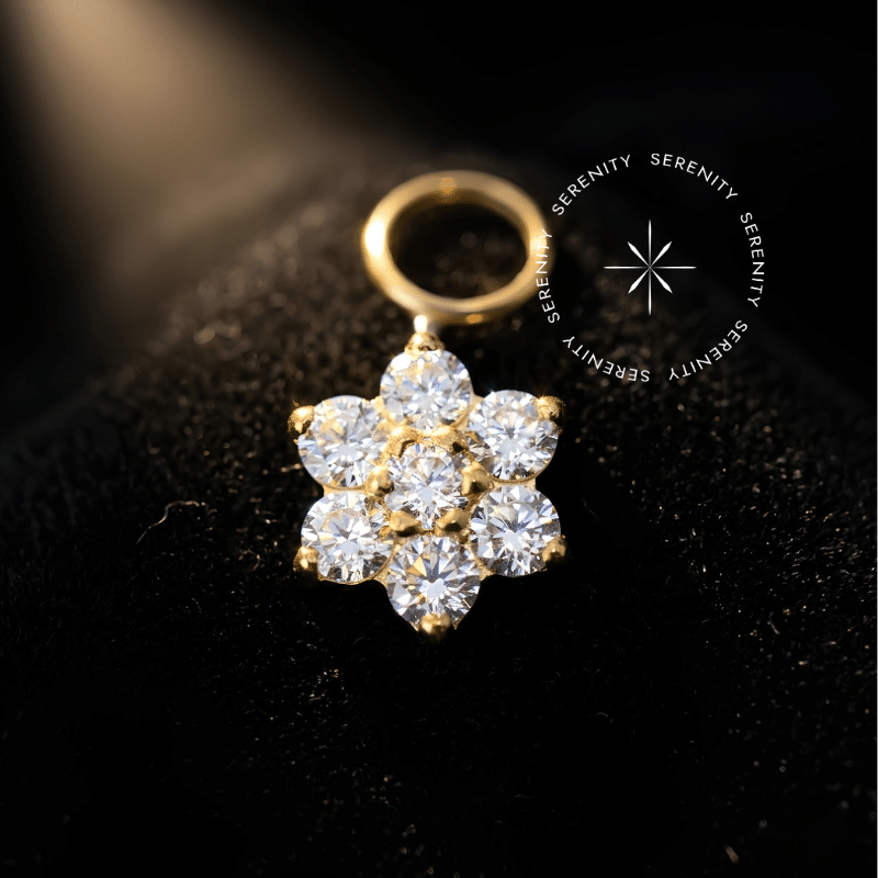 piercing titânio dourado formato de pingente flor, apresentando seis Zircônias Premium ao redor de um núcleo central, elo liso para acoplar em argolas, perfeito