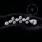 Topo Cluster Titânio Cravejado com três formações trinity e uma zircônia em gota, todas em zircônia translúcida brilhante, repousando suavemente sobre um tecido de cetim branco de alta opulência.