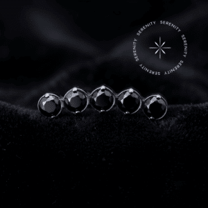 Piercing titânio grau implante modelo topo cluster cravejado com zircônias pretas de lapidação premium em titânio natural, repousando suavemente sobre um tecido de cetim branco de alta opulência.
