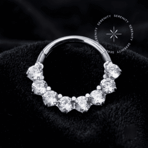 argola click titânio Argola click titânio cravejada frontalmente com 8 zircônias translúcidas em titânio grau implante natural, repousando suavemente sobre um tecido de cetim branco de alta opulência.
