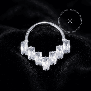 Piercing Argola Frontal triangular baguetes cravejada com zircônias translúcidas em titânio grau implante natural repousando suavemente sobre um tecido de cetim branco de alta opulência.