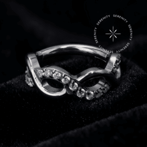 Piercing Argola infinito cravejada com zircônias translúcidas em titânio grau implante natural repousando suavemente sobre um tecido de cetim branco de alta opulência.