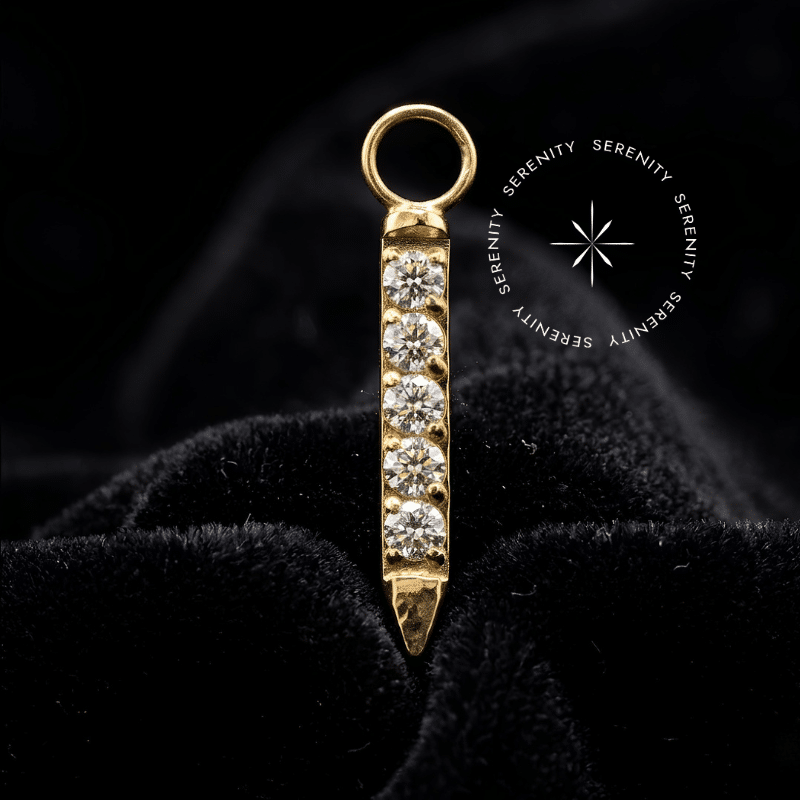 pingente titanio dourado em formato vertical (10.5mm) cravejado linearmente com Zircônias Premium Radiantes, argola superior lisa para fluidez de movimento em perfurações de hélix e lóbulo em alta joalheria.