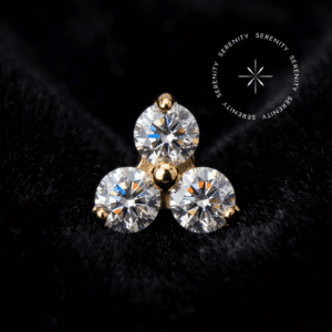 piercing titânio dourado modelo topo trinity cravejado com três zircônias de lapidação premium capturando a luz.