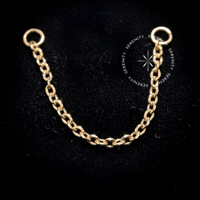 Corrente Piercing Titânio Dourado com elos encorpados de 0.8mm de espessura exibindo brilho reflexivo, finalizada com aros circulares vazados nas pontas, ideal para conexões luxuosas em furos de orelha.