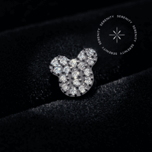 Piercing Titânio Grau Implante apresentando topo figurativo no formato Mickey Mouse de 6mm x 6.3mm totalmente cravejado com Zircônias Premium Translúcido Majestic. Possui pino de rosca interna de 0.9mm atraumático, fotografado em macro 8k sobre um suntuoso tecido de cetim branco puro para composição de alta joalheria auricular em Hélix, Tragus e Conch.