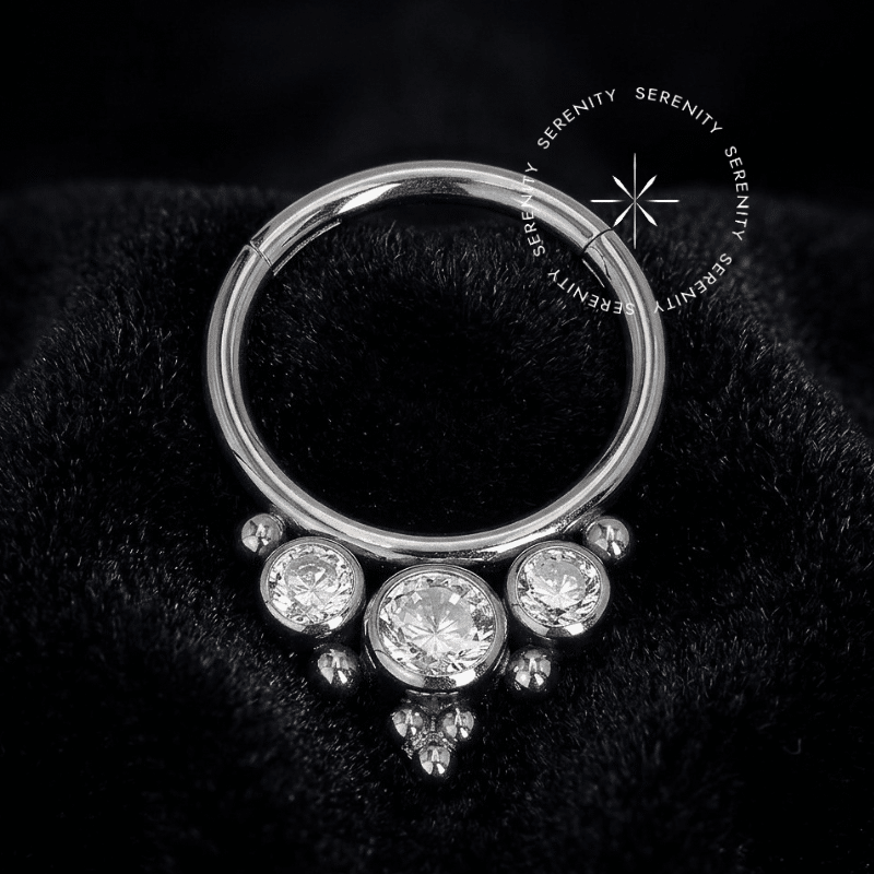 Piercing septo titânio TN2236 com design de argola segmento frontal cravejada com três zircônias premium radiantes intercaladas por esferas de metal polido, fechamento em clicker de precisão ideal para atualização estética de septo e daith.
