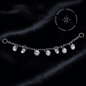 Corrente para Piercing modelo cravejada com sete zircônias translúcidas estruturadas em elos de titânio natural, repousando suavemente sobre um tecido de cetim branco de alta opulência.