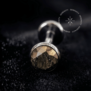 Piercing Topo para Labret em Titânio repousando suavemente sobre um tecido de cetim preto de alta opulência, destacando o polimento profundo e a gema marrom dourada.