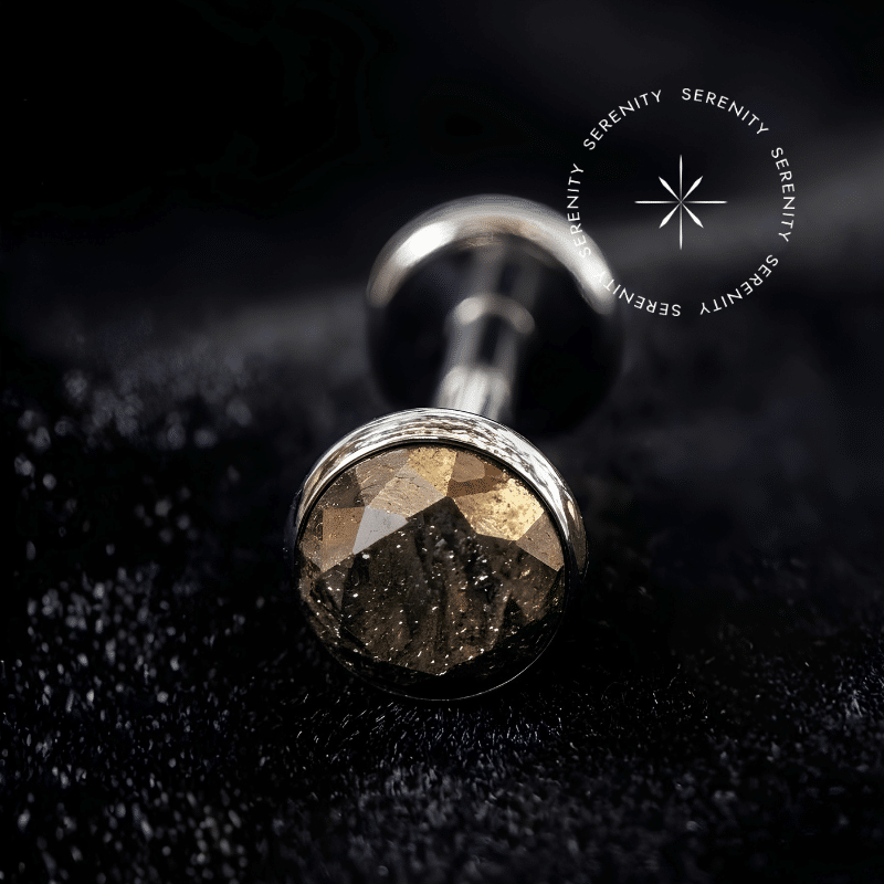 Piercing Topo para Labret em Titânio repousando suavemente sobre um tecido de cetim preto de alta opulência, destacando o polimento profundo e a gema marrom dourada.