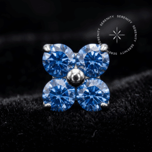 piercing rosca interna titânio modelo topo flor cravejada com zircônias de lapidação premium azul escuro, repousando suavemente sobre um tecido de cetim branco de alta opulência.