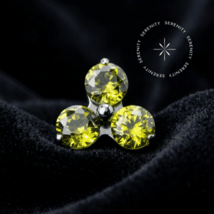 Topo Trinity Titânio apresentando design de três pontas cravejado com zircônias de lapidação premium na cor peridoto, repousando suavemente sobre um tecido de cetim branco de alta opulência.