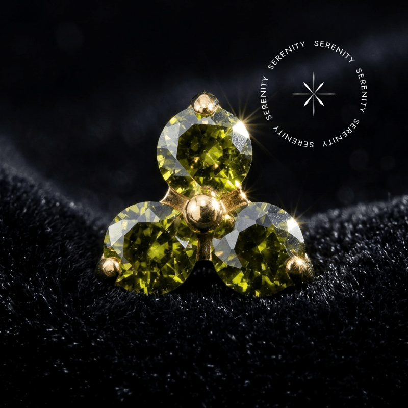 Topo Trinity Titânio Dourado apresentando design de três pontas com zircônias de lapidação premium na cor verde peridoto, destacando o encaixe push pin e o brilho do PVD Gold.
