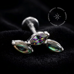 piercing titânio grau implante com design em cluster adornado por duas pedras naturais abalone e uma zircônia vitrail central repousando suavemente sobre um tecido de cetim branco de alta opulência.