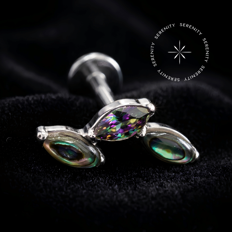 piercing titânio grau implante com design em cluster adornado por duas pedras naturais abalone e uma zircônia vitrail central repousando suavemente sobre um tecido de cetim branco de alta opulência.
