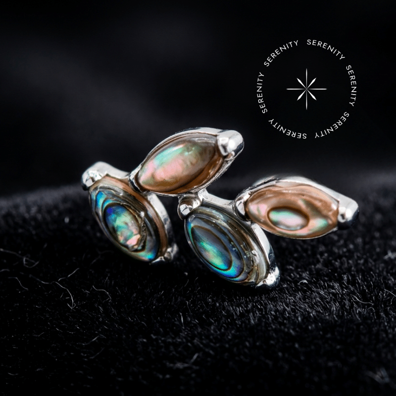 piercing titânio grau implante com design em cluster de 11mm adornado por quatro autênticas pedras naturais abalone, repousando suavemente sobre um tecido de cetim branco de alta opulência.
