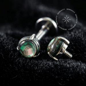 piercing titânio grau implante com topo circular minimalista de 3mm adornado por autêntica pedra natural abalone, repousando suavemente sobre um tecido de cetim branco de alta opulência.