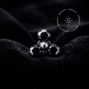 Piercing Labret modelo topo trinity cravejado com três zircônias pretas estruturadas em titânio natural, repousando suavemente sobre um tecido de cetim branco de alta opulência.