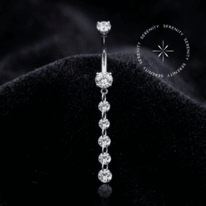 Piercing Umbigo Pingente Titânio repousando suavemente sobre um tecido de cetim branco de alta opulência, evidenciando o brilho profundo de suas zircônias translúcidas e o acabamento espelhado impecável do titânio natural platinado.