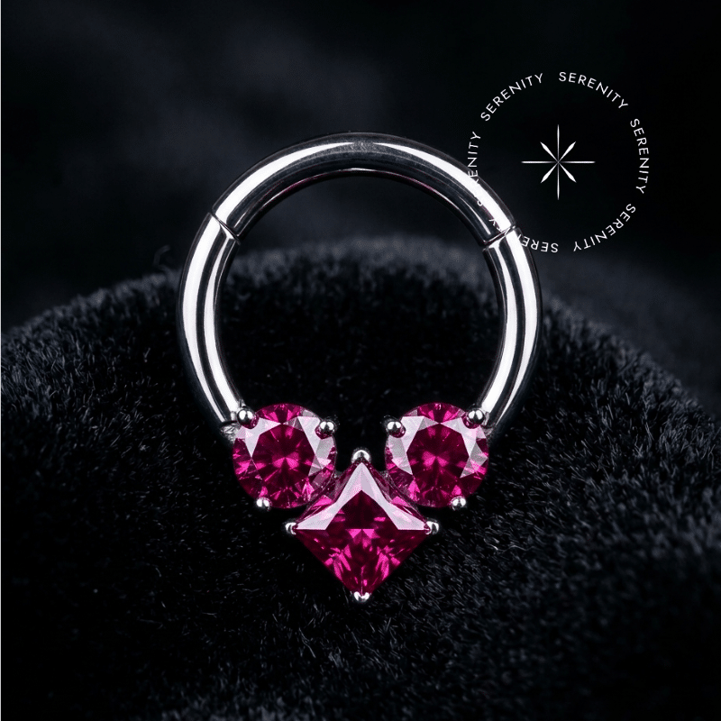 piercing septo titânio com design de argola clicker adornado por três zircônias rosa pink de lapidação premium, repousando suavemente sobre um tecido de cetim branco de alta opulência.