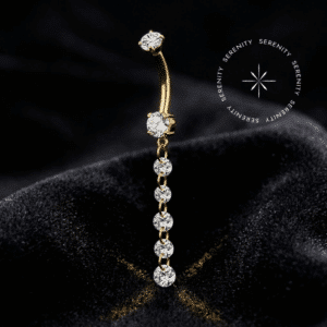 Piercing Umbigo Pingente Titânio repousando suavemente sobre um tecido de cetim preto de alta opulência, evidenciando o brilho profundo de suas zircônias e o acabamento espelhado do revestimento em ouro 18k.